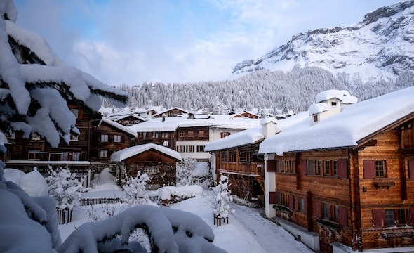 a group of snow covered buildings with snow dusted trees and mountainous terrain in the background